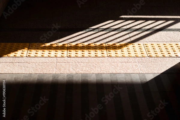 Obraz 駅構内の点字ブロックと影　バリアフリーの通路背景