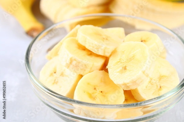 Fototapeta Bananas are whole and cut on a slice in a cup on a gray background.