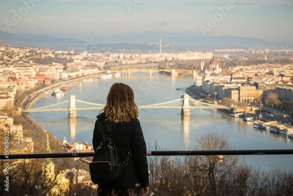 Fototapeta Young woman is looking at the Chain bridge, Budapest parliament and cityscape from The Citadella which is a fortification located upon the top of Gellert Hill in Budapest, Hungary.