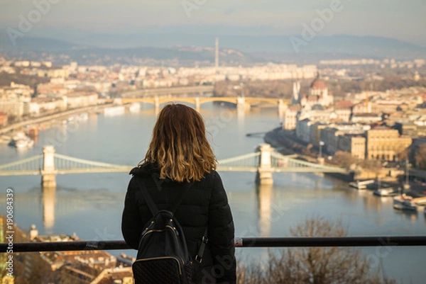 Fototapeta Young woman is looking at the Chain bridge, Budapest parliament and cityscape from The Citadella which is a fortification located upon the top of Gellert Hill in Budapest, Hungary.
