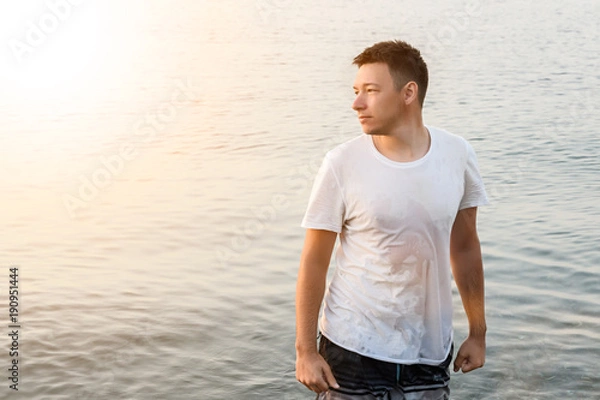 Fototapeta a man stands in the drenched white t-shirt and looks away clenching his hands into fists