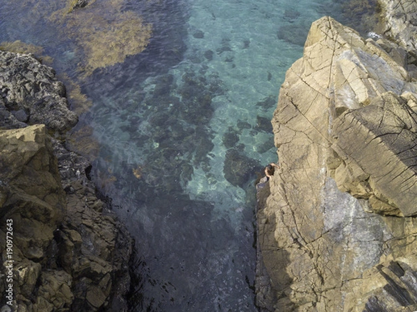 Fototapeta drone shot of a man climbing a rock in the ocean