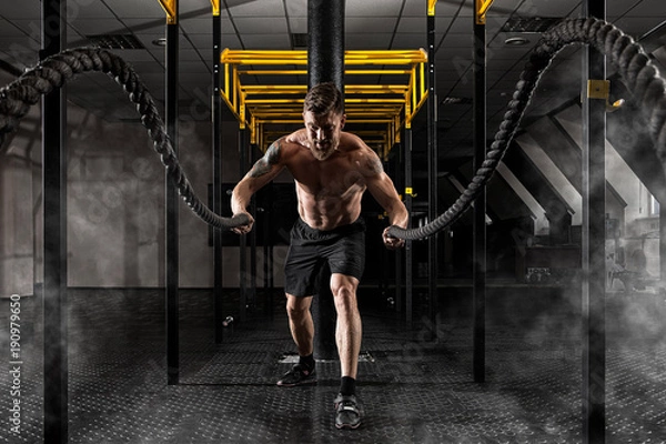 Fototapeta Man working out with battle ropes at gym