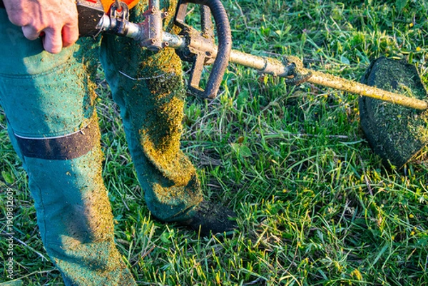 Obraz Worker Cutting Grass with Brush Cutter at Sunset
