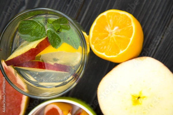 Fototapeta A glass of detox water with slices of fresh apple, lemon and a spring of mint, black wooden background, top view