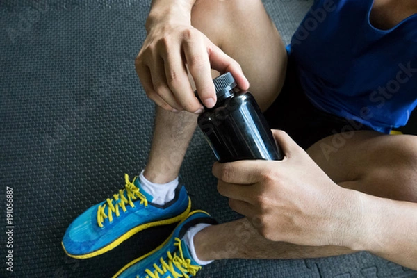 Fototapeta Sport man opening the bottle of pills in the gym