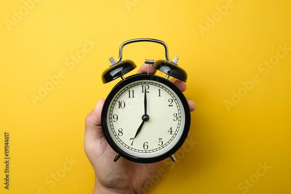 Fototapeta men holding black alarm clock in one hand on yellow background color