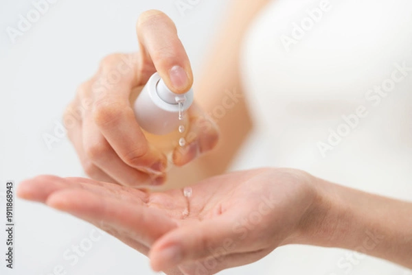 Obraz スキンケアプロセス。ポンプ式容器、美容液、化粧水を手元に出している女性の手元。