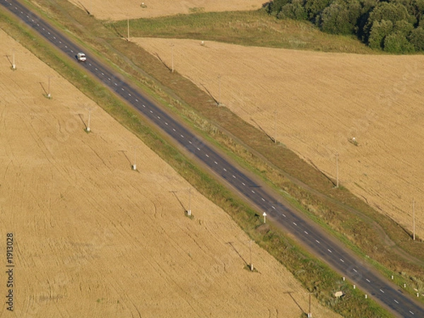 Fototapeta road across field with telegraph pole with automobile.