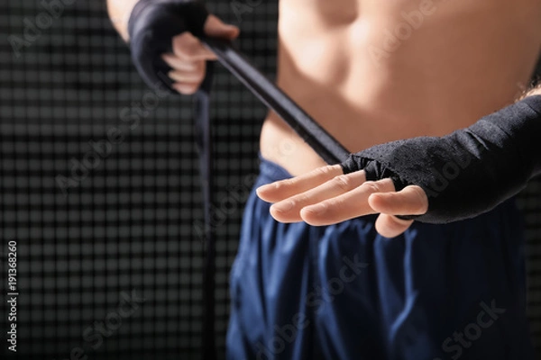 Fototapeta Young boxer applying wrist wraps in gym, closeup