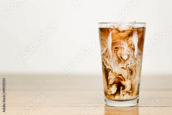 Obraz Iced coffee on a wood table with cream being poured into it showing the refreshing drink with a clean background