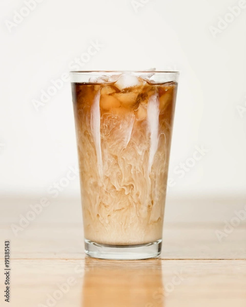 Obraz Iced coffee on a wood table with cream being poured into it showing the refreshing drink with a clean background