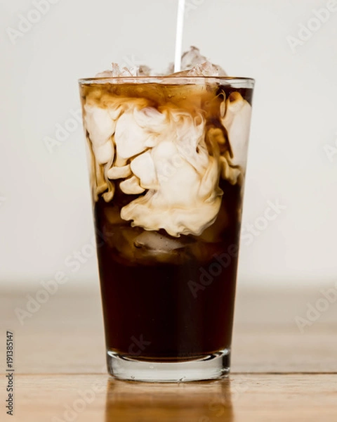 Obraz Iced coffee on a wood table with cream being poured into it showing the refreshing drink with a clean background