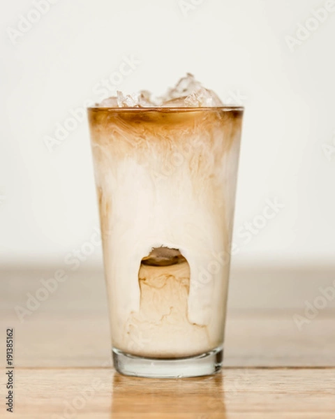 Obraz Iced coffee on a wood table with cream being poured into it showing the refreshing drink with a clean background