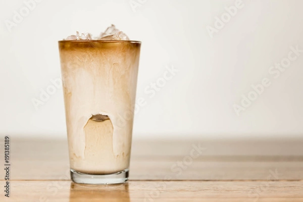 Obraz Iced coffee on a wood table with cream being poured into it showing the refreshing drink with a clean background