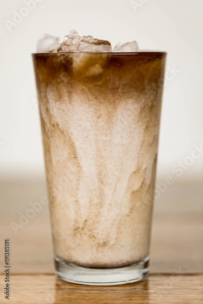 Obraz Iced coffee on a wood table with cream being poured into it showing the refreshing drink with a clean background