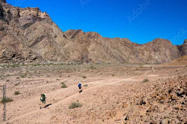 Fototapeta Two hikers walking long a path in the desert of the Fish River Canyon in Namibia