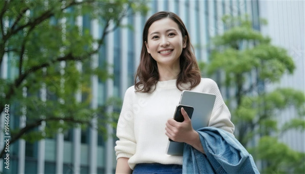 Obraz 新緑のオフィス街をパソコンを抱え立つビジネス女性