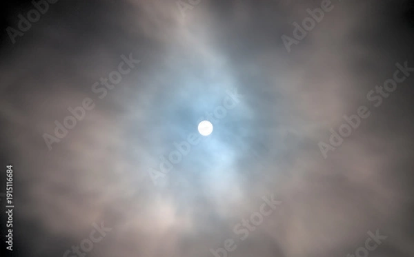 Obraz A dramatic sky with thick clouds partially covering the sun