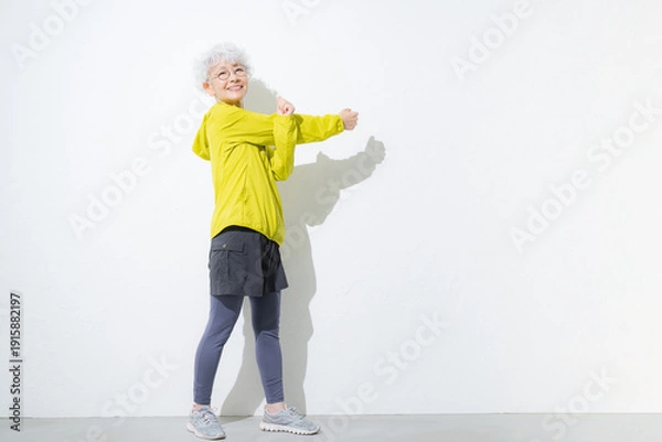 Obraz 白背景でスポーツウェアでストレッチで腕を伸ばすグレイヘアのシニア女性の全身
