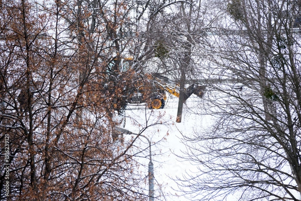Obraz Snow-covered landscape with a working machine clearing the path