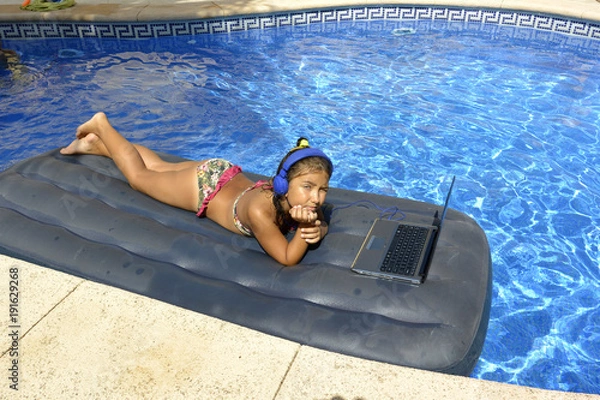 Obraz A girl in bikini with computer and headphones sunbathing on an inflatable mattress in the pool