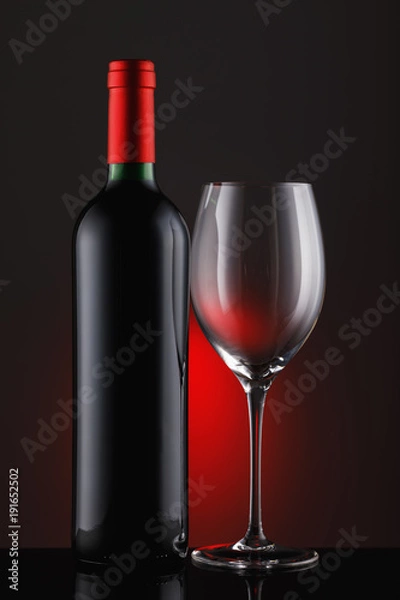 Obraz  Bottle of red wine with an empty glass on a black background, vertical close-up image