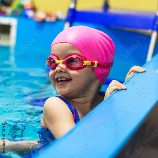 Fototapeta A little girl of European appearance in glasses in the pool, smiling and looking at camera