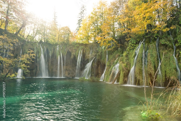 Obraz Multiple waterfalls show the different heights of the lakes in Plitvice Lake National Park. The trees are golden yellow and the water is clear and turquoise.
