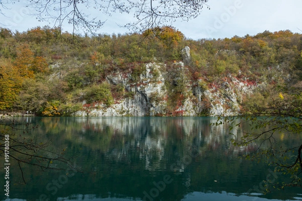 Obraz White cliffs in Plitvice Lakes National Park with a few tree branches in the shot. The reflection of the white cliffs can be seen in the still water. 
