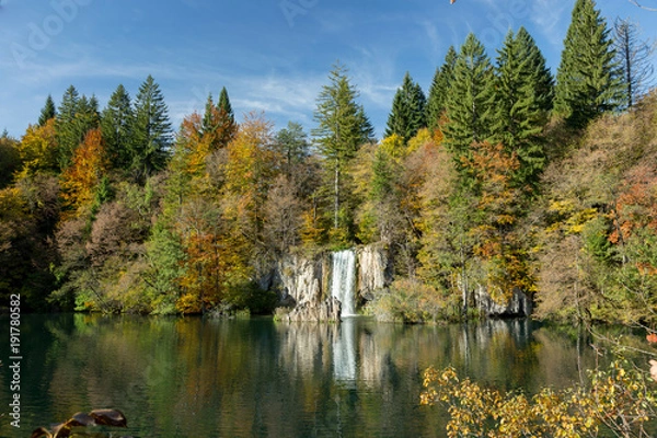 Obraz A waterfall and a lake in Croatia. The sky is mostly clear with few clouds and the trees are green and yellow. Taken at Plitvice Lakes National Park.