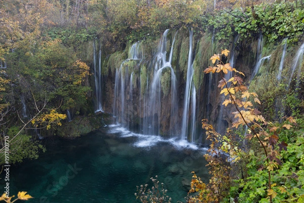 Obraz Long exposure of a waterfall in Plitvice Lakes National Park. There is lush foliage surrounding the waterfall and the water is crystal clear turquoise blue. 