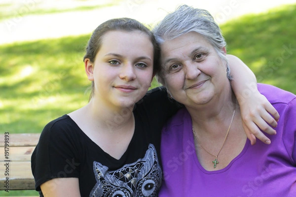 Obraz Happy family, generation and people concept - happy smiling young twelve years old granddaughter with senior grandmother standing  at Summer Park , hugging in Oregon USA close-up portrait 