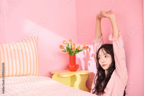 Obraz ピンク背景の部屋でリラックスするアジアの若い女性のポートレート