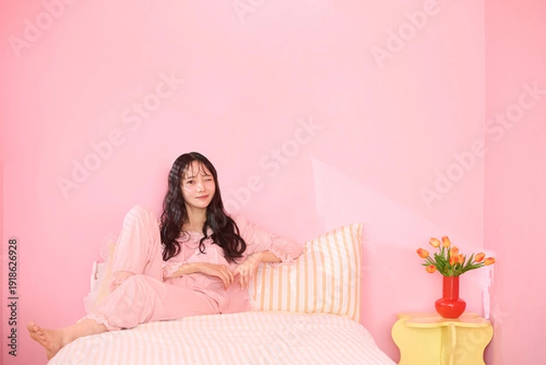 Obraz ピンク背景の部屋でリラックスするアジアの若い女性のポートレート