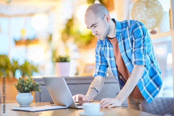 Fototapeta Young man in casualwear leaning over table while networking at home