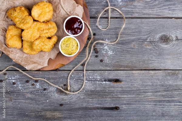 Fototapeta Wooden board with tasty chicken nuggets and sauces on table