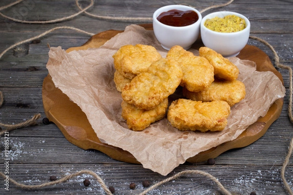 Obraz Deska drewniana z pysznymi bryłkami kurczaka i sosami