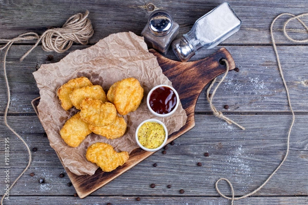 Fototapeta Wooden board with tasty chicken nuggets and sauces on table