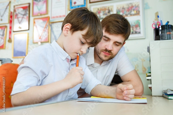 Fototapeta Little boy doing home work in his room with tutor. Adult man helping child concept