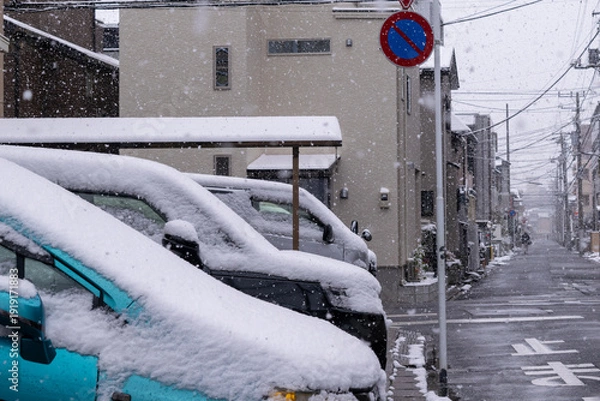 Obraz 雪が降る街角の路地の駐車場の車に積もる雪