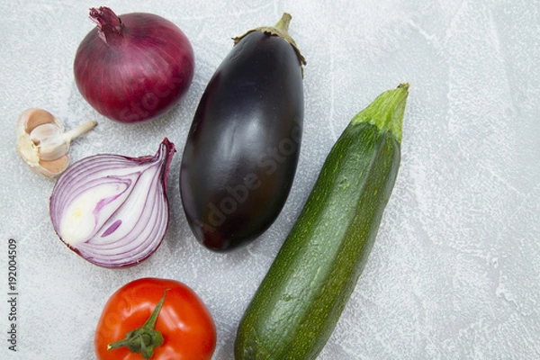 Fototapeta Set of raw ingredients for Italian cooking on stone table background. Eggplant, garlic, onion, tomato, zucchini. Closeup and top view