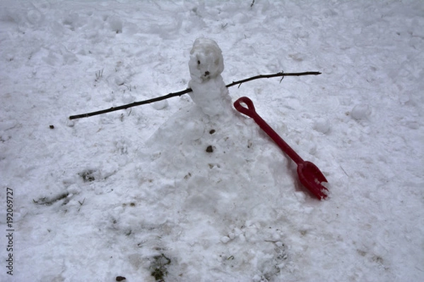 Obraz A terrible and ugly snowman made by children in the winter courtyard of a private house on the day of vacation and festive mood against the background of white and dirty snow.