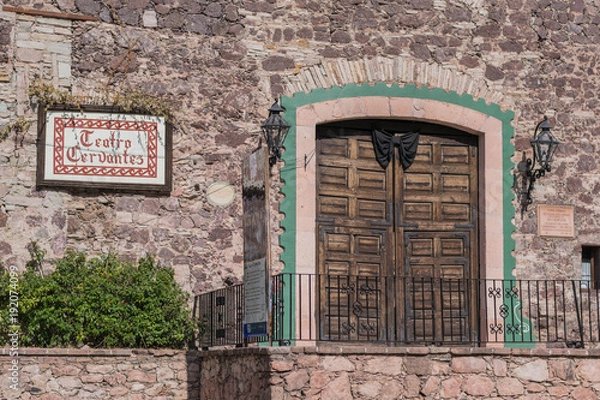 Fototapeta Old stone building, with the  front entrance of the Teatro Cervantes, with double wooden carved doors, a stone door frame, iron railing and theater sign, in Guanajuato, Mexico
