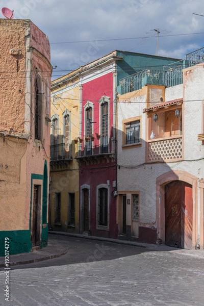 Fototapeta Street scene with a curve corner building painted yellow and green, a cobblestone street and other architectural details, in Guanajuato, Mexico