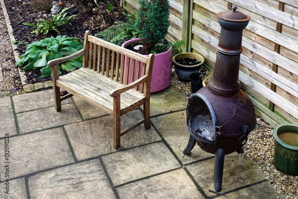 Obraz Wooden bench, chiminea and various plants, some in pots, in a small domestic courtyard garden in winter
