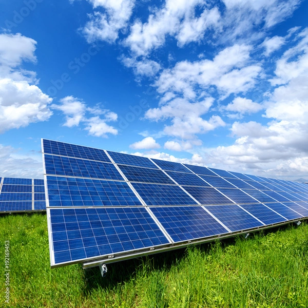 Fototapeta Solar panel on blue sky background. Green grass and cloudy sky. Alternative energy concept