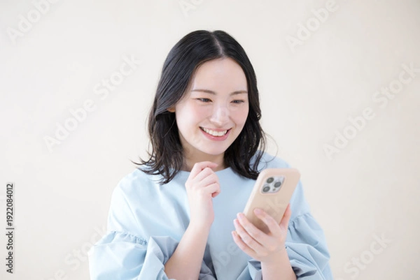 Obraz スマホを操作する笑顔の女性 　オンライン利用・サービスなどの口コミや申し込みをするイメージ　スマホを見る