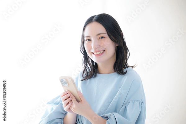 Obraz スマホを操作する笑顔の女性 カメラ目線　オンライン利用・サービスなどの口コミや申し込みをするイメージ