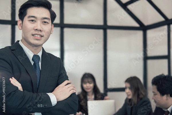Fototapeta asian businessman smiling at camera while colleagues have meeting at office. business people working with co worker team